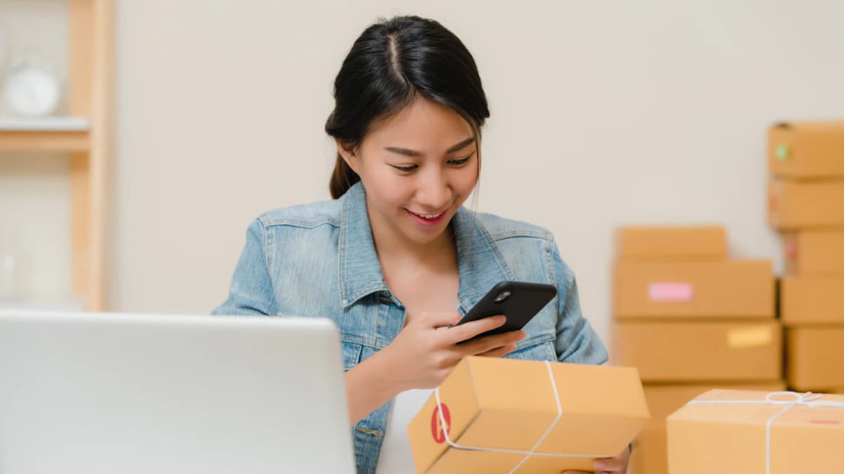 A seller packing an order while checking it on her phone